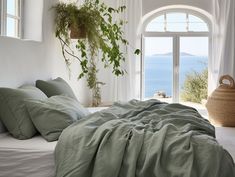 an unmade bed with green sheets and pillows in front of a window overlooking the ocean