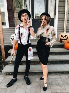 two people dressed up as zombies on the front steps of a house with pumpkins