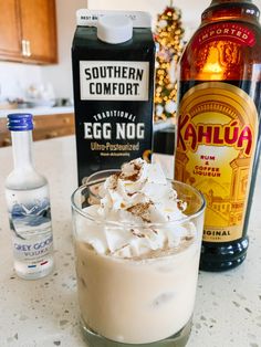 an egg nog drink with whipped cream in a glass next to two bottles of booze