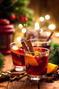 two glasses filled with mulled drink and cinnamon sticks on a table next to christmas decorations