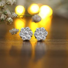 a pair of diamond earrings sitting on top of a wooden table next to white flowers