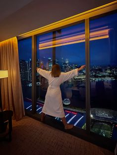 a woman standing in front of a window looking out at the cityscape outside