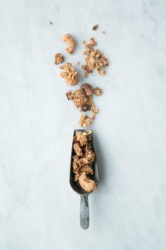 an ice cream scoop full of granola and walnuts on a marble counter top