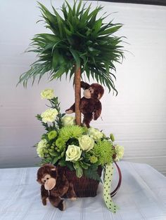 a stuffed bear sitting in a basket with flowers and greenery next to a palm tree