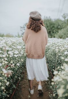 a woman walking through a field of white flowers