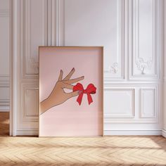 a hand holding a red bow in front of a pink wall with white paneling