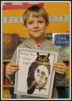 a young boy holding up a poster with an owl on it in front of bookshelves