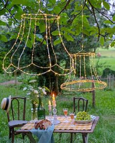 two chandeliers hanging from a tree in the middle of a yard with food and wine