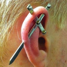 the man is getting his ear pierced with two small metal crosses attached to it's side