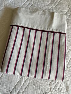 a white bed with red and blue striped sheets on it's side, next to a pillow