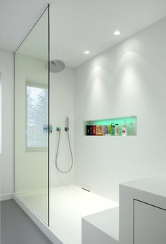 a bathroom with a glass shower door and white counter top, along with an illuminated shelf on the wall