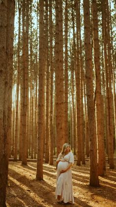 a pregnant woman standing in the middle of a forest holding her belly up to her chest