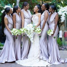 a group of women standing next to each other in front of flowers and greenery