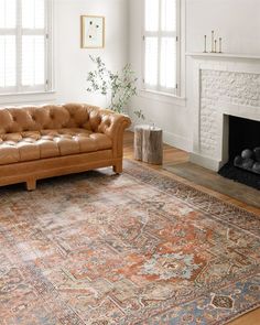 a living room with a couch, fireplace and rug on the floor in front of two windows