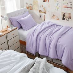 a bed with purple sheets and pillows in a bedroom next to a dresser, window and pictures on the wall