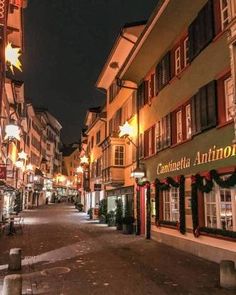 an empty street in the middle of town at night with christmas decorations on the windows