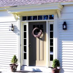 a wreath on the front door of a house with two potted plants in front