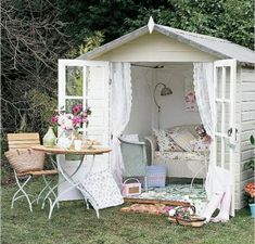 a white garden shed sitting on top of a lush green field next to a table and chairs