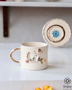 a white coffee cup sitting on top of a table next to a plate and flower