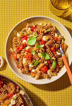 a bowl of pasta with tomatoes, basil and cheese on a yellow tablecloth next to a glass of wine