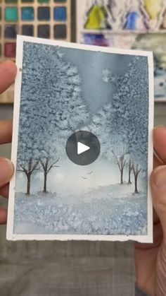 a person holding up a card with an image of trees in the snow on it