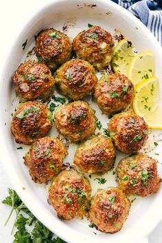 cooked meatballs in a white dish with lemon wedges and parsley