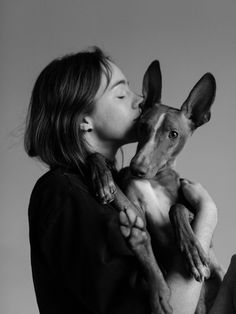 a woman is kissing a dog with her face close to the camera while it's being held by its owner