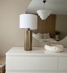 a mirror sitting on top of a white dresser next to a lamp and a basket