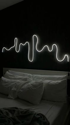 a bed with white sheets and pillows under a neon sign on the wall above it