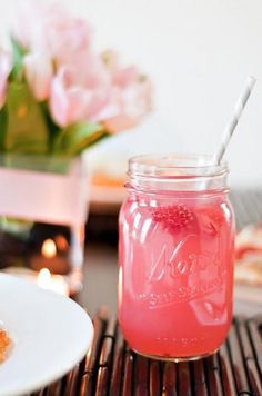 a mason jar filled with pink liquid sitting on top of a table next to a plate