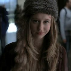 a young woman wearing a fur hat and looking at the camera while standing in an airport