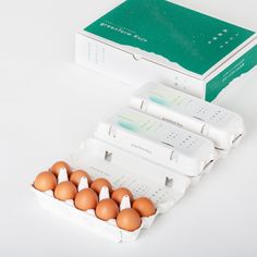 six eggs are in an egg carton on a white surface next to a green box