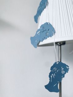 some blue paper cutouts hanging from a lamp shade on a white wall with a person's head