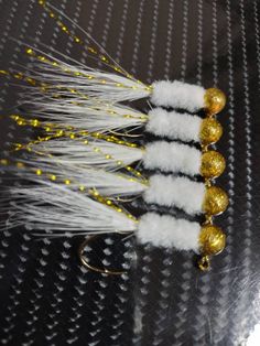 three white and gold lures on a black table with some yellow balls in the background