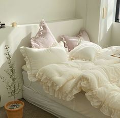 an unmade bed with white sheets and pink pillows on top of it next to a potted plant