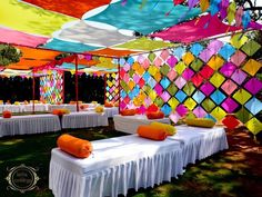 an outdoor event with tables covered in white linens and bright colored cloths hanging from the ceiling