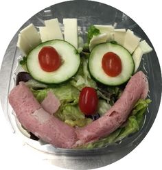 a salad with cucumbers, cheese and meat in the shape of a face