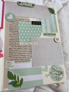 an open scrapbook with paper and stickers on it's cover, sitting on a bed