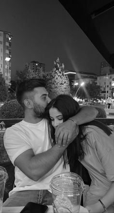 a man and woman sitting at a table with their arms around each other in black and white