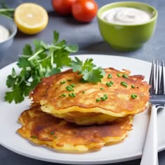 two pancakes on a white plate with parsley next to the plates and bowls of sauce