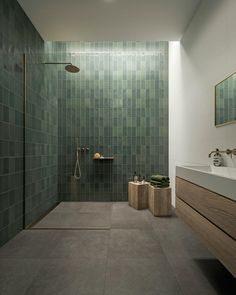 a modern bathroom with green tile on the walls and floor, along with a walk in shower