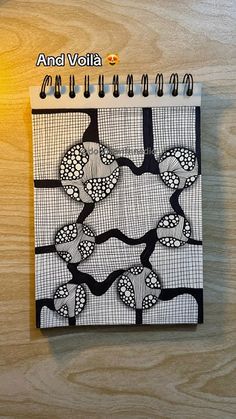 a spiral notebook with black and white designs on the cover, sitting on a wooden surface