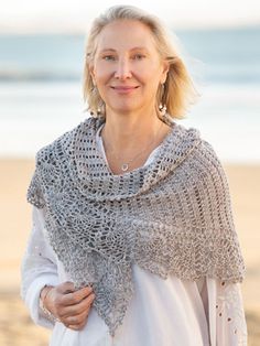 a woman standing on the beach wearing a crocheted shawl