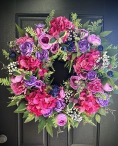 a wreath with purple and pink flowers hanging on a door