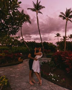 a man and woman embracing each other in front of palm trees