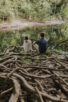 two people sitting on the edge of a river surrounded by tree roots