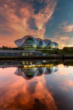 an image of a building that is reflecting in the water at sunset or sunrise time