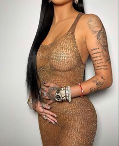 a woman with long black hair and tattoos on her arm, wearing a brown dress