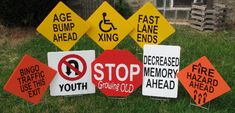 various road signs sitting in the grass near a house