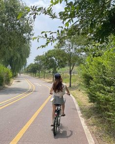 a woman riding a bike down the middle of a road with trees on both sides